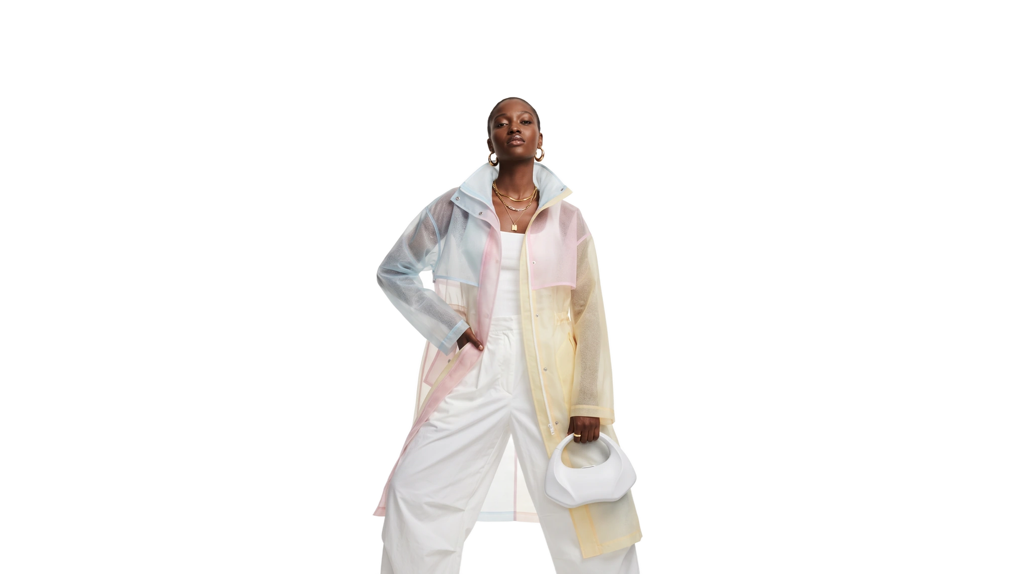 A model in a translucent colour-block raincoat in pale blue, pink and yellow over white trousers, holding a small white bag, cut out on a plain ground